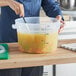 A person mixing food in a large clear plastic container with a black handle.