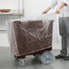 A man holding a plastic wrap over a brown Cambro dish caddy.