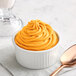 A bowl of orange soft serve with a spoon on a table.