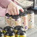 A woman's hand holds a stack of cans in a black plastic PakTech 6-pack carrier with money inside.