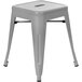 A silver metal stackable backless stool with a square drain seat.