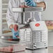 A person in a white coat and blue gloves using an Avantco meat grinder on a counter.