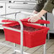 A person putting food into a red Choice meat lug container.