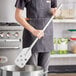 A man in a kitchen using a Fourt&#233; stainless steel paddle to stir a pot.