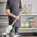 A man in an apron using a Fourt&#233; stainless steel paddle over a pot on a stove.