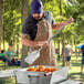 A man in an apron using a Fourt&#233; stainless steel paddle to cook food on a grill.