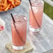 Two glasses of blueberry lemonade with straws on a marble table.