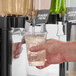 A hand holding a glass of ice with green liquid made from Pure Craft Beverages Ginger Pear Beverage Concentrate.