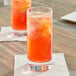 A glass of red liquid with orange liquid and ice on a table.