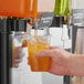 A hand holding a plastic cup of green liquid in front of a Pure Craft Beverages Pineapple Papaya Beverage Concentrate bottle.