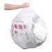 A person's arm holding a white plastic bag of Lavex trash bags.