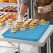 A person in gloves holding a blue MFG Fiberglass Market Display Tray of cupcakes.