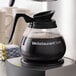 An Avantco Equipment glass coffee decanter with a black handle on a counter.