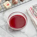 A bowl of red liquid next to chocolates on a wire rack.