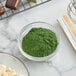 A bowl of Roxy & Rich green fat dispersible powder on a marble surface.