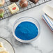 A bowl of Roxy & Rich Brilliant Blue powder next to a plate of chocolates.