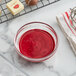 A white bowl of red liquid next to a bowl of chocolate.