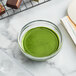 A bowl of green liquid on a brown surface.