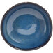 A blue ramekin with a white interior on a blue surface.