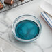 A bowl of blue liquid next to a tray of chocolates.