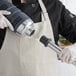 A person in a chef's uniform using an AvaMix heavy-duty immersion blender to mix in a metal cylinder.