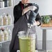 A man using an AvaMix heavy-duty immersion blender to mix green liquid in a large black and silver bowl.