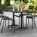 A Lancaster Table & Seating black aluminum outdoor table with chairs and a black umbrella on a patio.