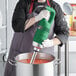 A person using an AvaMix immersion blender to mix tomato sauce in a pot.