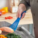 A person holding a blue Mercer Culinary High Temperature slotted spatula over food.