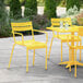 A yellow Lancaster Table & Seating outdoor arm chair on a patio with a yellow table and two glasses of water.