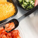 A person using a Thunder Group black polycarbonate salad bar spoon to serve tomatoes.