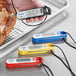 A hand holding a yellow AvaTemp digital folding probe thermometer over a piece of meat.