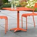 A Lancaster Table & Seating orange outdoor table with chairs on a patio.