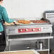 A person cooking food on a large Avantco countertop electric griddle.