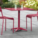 A Lancaster Table & Seating red powder-coated aluminum table with two chairs on an outdoor patio.