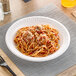 A Dart Concorde white foam plate with spaghetti and meatballs on it.