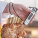 A person holding an AvaTemp black digital folding probe thermometer over a piece of meat.