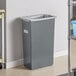 A Lavex gray rectangular trash can on a shelf with a bag inside.