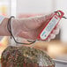 A person using an AvaTemp red digital folding probe thermometer to measure meat.
