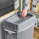 A person using a Lavex gray slim rectangular trash can drop shot lid to throw away paper on a counter.