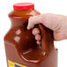 A hand holding a gallon of Louisiana Wildly Wicked Original Buffalo Wing Sauce with a red cap.