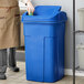 A man in a chef's outfit standing next to a blue Toter Slimline trash can.