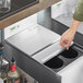 A hand using a Regency stainless steel sliding lid to cover an ice bin.
