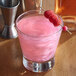 A glass of pink drink with Spirdust Pink Cocktail Shimmer and raspberries on a toothpick.