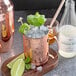 a copper mug with ice and mint leaves on a wooden board