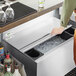 A person sliding a stainless steel lid onto a Regency underbar ice bin.