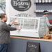 An open Avantco white countertop bakery display case full of food with a man standing next to it.