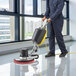 A man in a blue uniform using a Lavex single speed rotary floor machine to clean a floor.