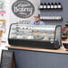 An Avantco black refrigerated countertop bakery display case on a counter filled with cakes and desserts.