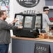 An Avantco countertop bakery display case on a counter in a bakery with a man in a white shirt taking food.